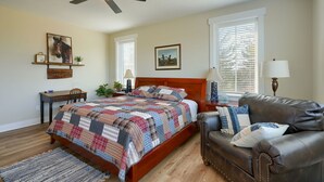 A bedroom with a bed, a ceiling fan, a wooden headboard, a leather couch, and a window with blinds. - Heavenly View | Hocking Hills, Pool, Theater (Logan)
