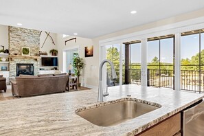 A modern kitchen with a large sink, a dining area, and a living room with a fireplace. - Heavenly View | Hocking Hills, Pool, Theater (Logan)