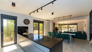 A modern kitchen with a central island, a dining area with green chairs, and a view of the outdoors. - Stunning home in Zaton with private swimming pool, can be inside or outside (Zaton)