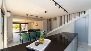 A modern kitchen with a central island, a dining area with green chairs, and a staircase with a railing. - Stunning home in Zaton with private swimming pool, can be inside or outside (Zaton)