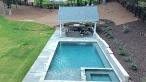 A rectangular swimming pool with a built-in hot tub, surrounded by stone tiles. - Spacious Lake House with Dock and Swimming Pool (Dawsonville)