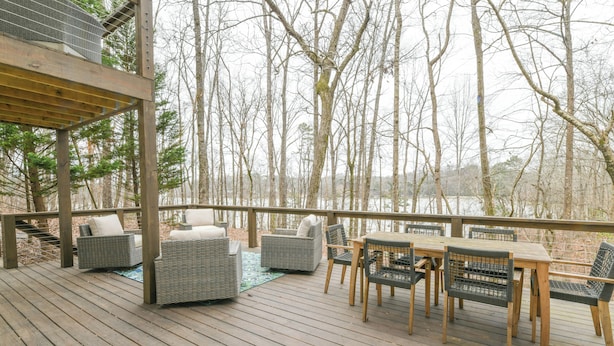 A wooden deck with outdoor furniture, including sofas and chairs, overlooking a forested area. - Spacious Lake House with Dock and Swimming Pool (Dawsonville)