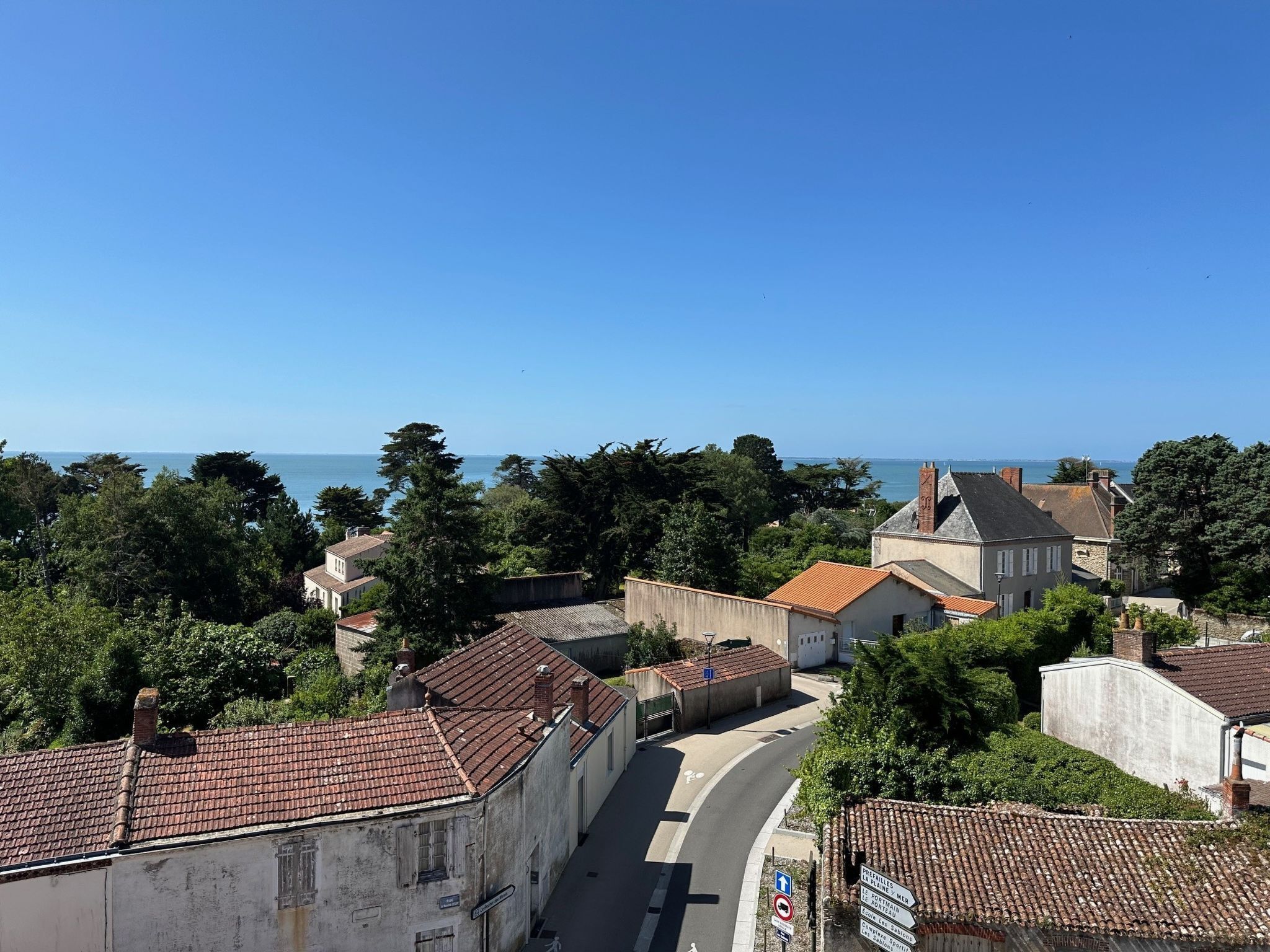Une ville côtière dont les bâtiments se distinguent par leurs toits recouverts de tuiles rouges, une rue sinueuse et une vue sur la mer.