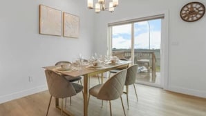 A dining area with a table set for four, a chandelier, and a large window with a view. - Secord Serenity (Edmonton)