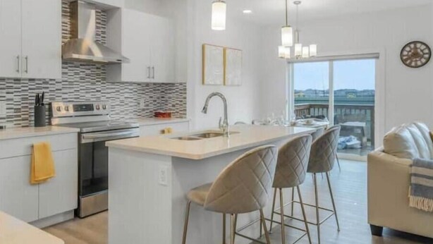 A modern kitchen with white cabinets, a central island, and pendant lighting. - Secord Serenity (Edmonton)