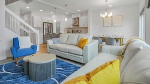 A modern living room with a staircase, a dining area, and a kitchen. - Secord Serenity (Edmonton)