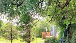 Un sendero de jardín que conduce a una pérgola de madera con una mesa y sillas, rodeada de abundante follaje y árboles.