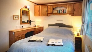 Un dormitorio con cama, cómoda de madera, espejo y lámpara de noche.