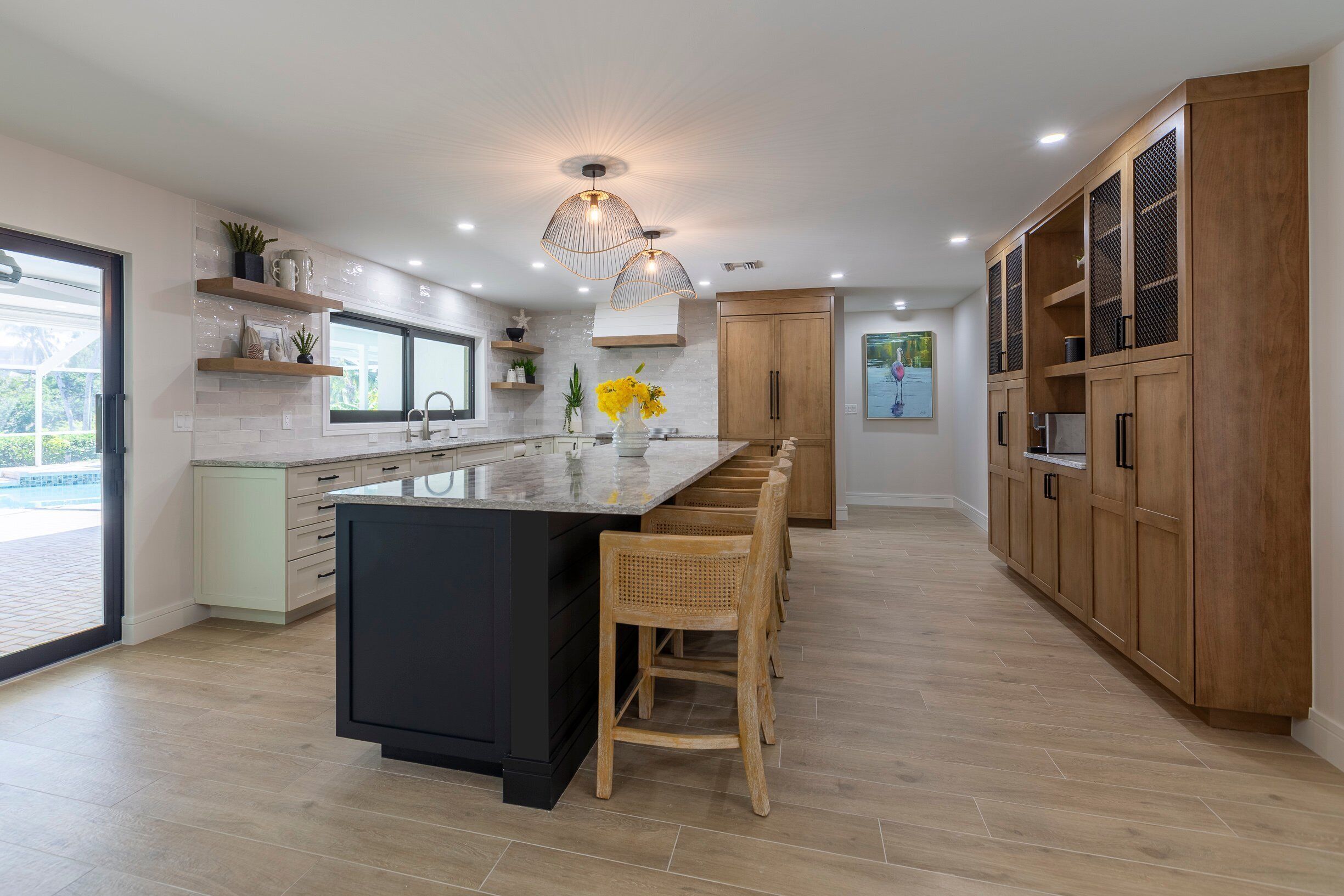 A modern kitchen with a large island, wooden cabinets, and a view to the outside.