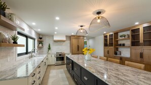 A modern kitchen with a marble countertop, wooden cabinets, and pendant lighting. - Stunning Canal Front Home Exquisite Design! (Sanibel)