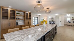A modern kitchen with marble countertops, wooden cabinets, and pendant lighting. - Stunning Canal Front Home Exquisite Design! (Sanibel)