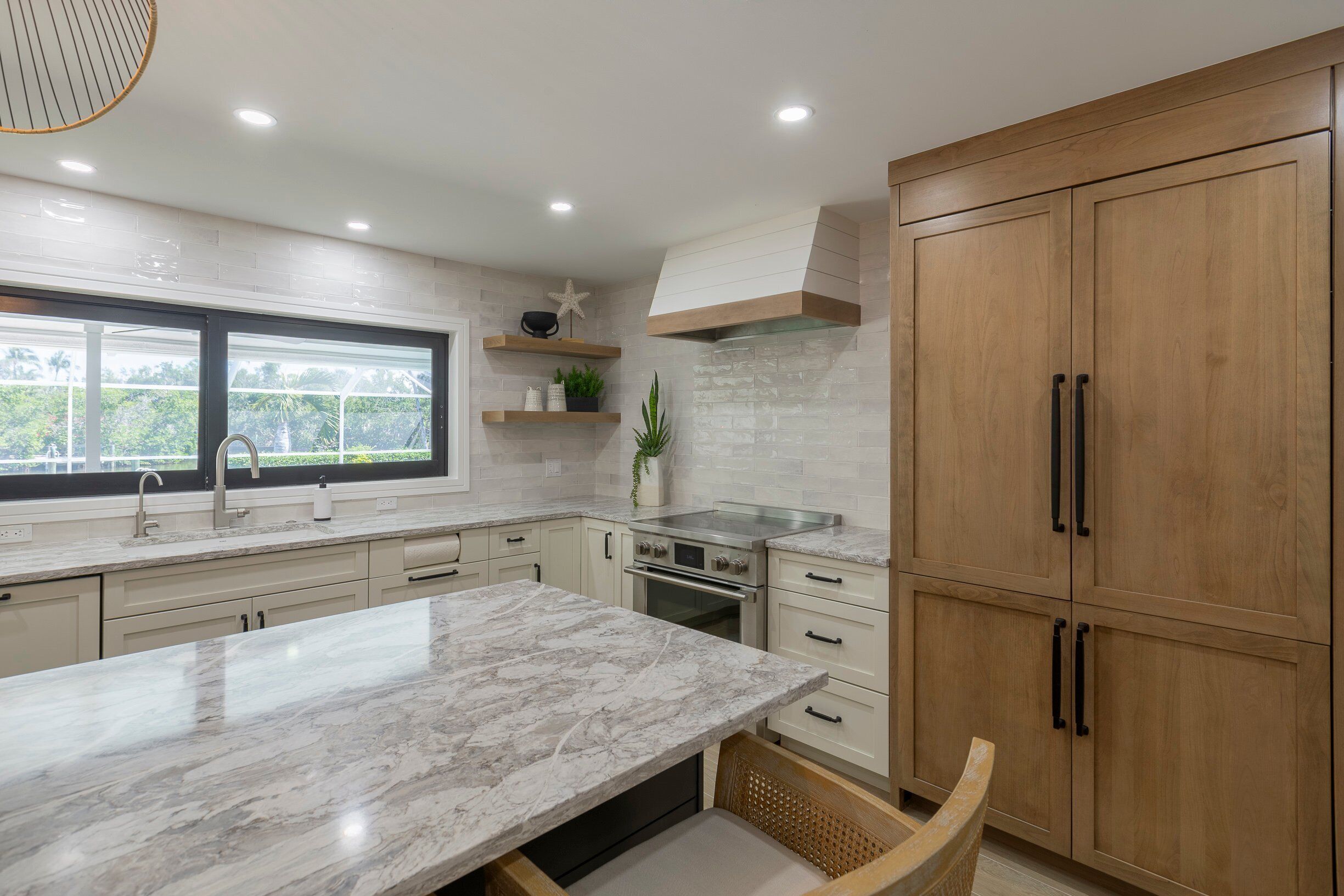A modern kitchen with a marble countertop, wooden cabinets, and a large window.