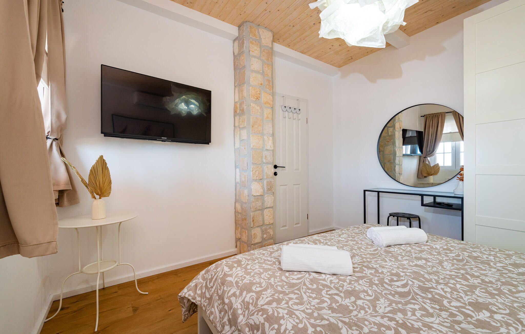 A bedroom with a bed, a TV, a stone wall, a mirror, and a small table.