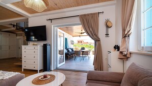 Ein modernes Wohnzimmer mit Flachbildfernseher, einem weißen Sofa, einem Couchtisch und einem Essbereich mit Sitzgelegenheiten im Freien.
