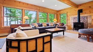 Un salon chaleureux avec un canapé, des fauteuils et une table basse. Il y a de grandes fenêtres, une cheminée et un mur en pierre.