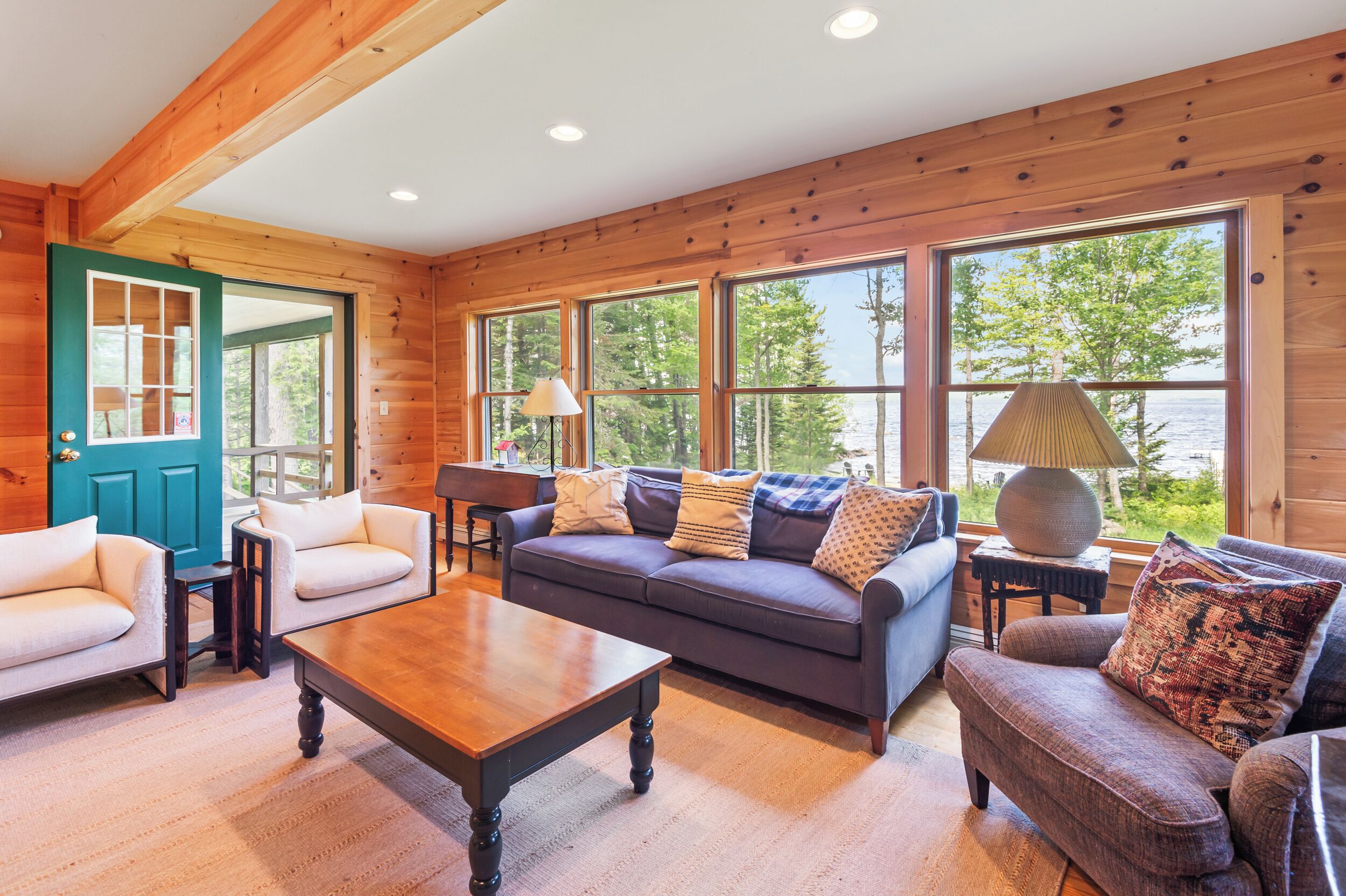 A cozy cabin interior with a wooden interior, a sofa, a coffee table, and large windows offering a view of the outdoors.