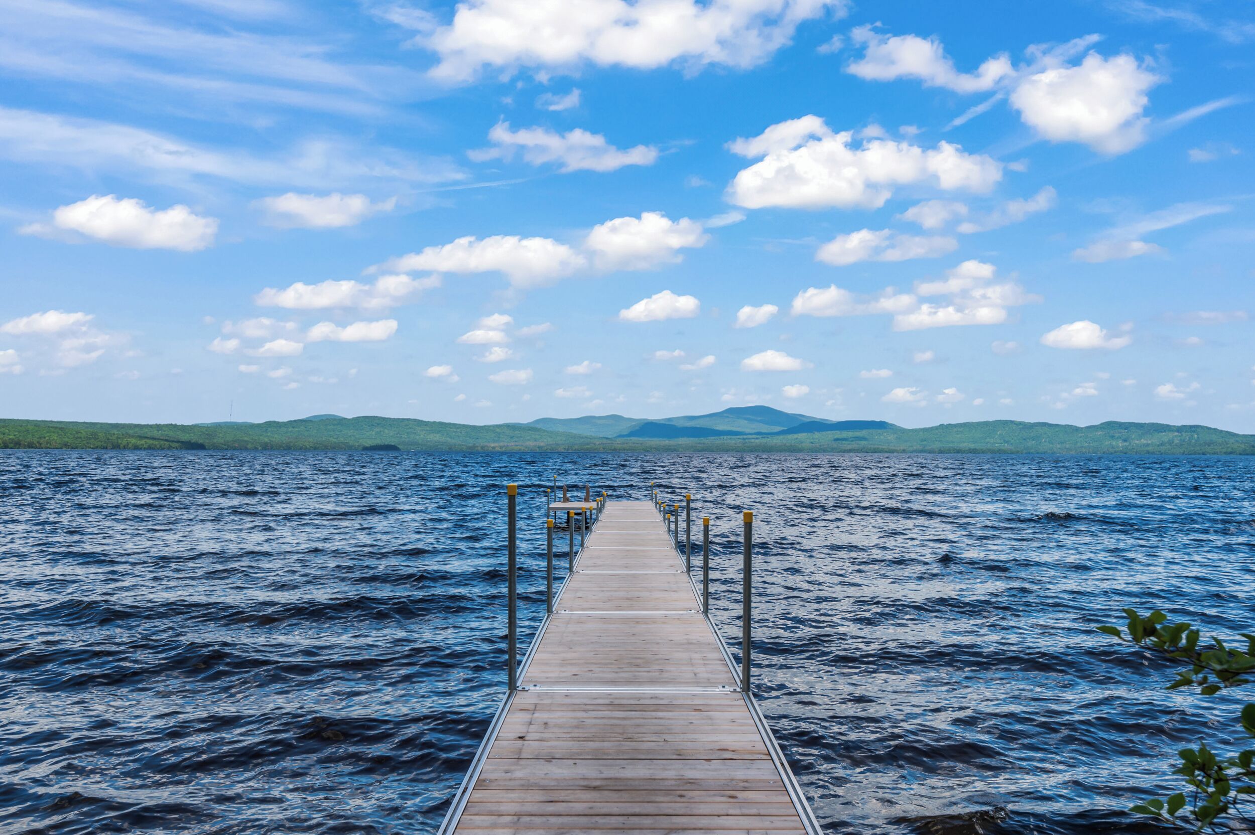 A wooden pier extending into a large body of water with mountains in the background.