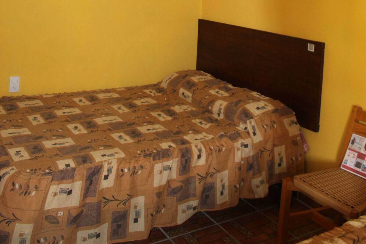 A room with a bed, a ceiling fan, and a wooden chair.
