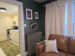 A living room with a brown leather sofa, a radiator, and framed pictures on the wall. - Stylish Apt in Walker's Point (Milwaukee)