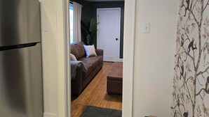 Un couloir menant à un salon équipé d’un canapé, d’une porte et d’un réfrigérateur.