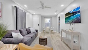 A modern living room with a grey sofa, a yellow armchair, a dining table, and a TV on the wall.