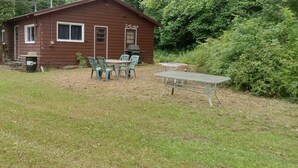 A rustic cabin with a small patio area, a grill, and outdoor seating.