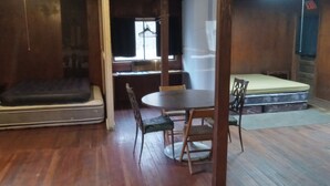A room with a wooden floor, a bed, a dining table with chairs, and a small kitchenette area.