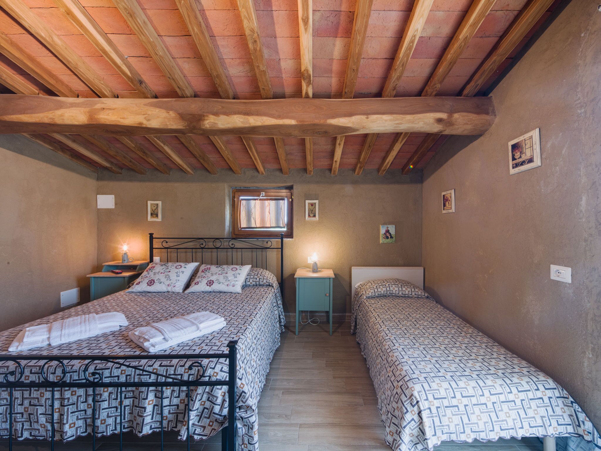 A cozy bedroom with two beds, wooden beams on the ceiling, and a window with curtains.