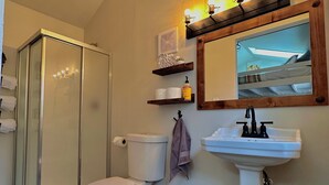 Un baño con cabina de ducha de vidrio, inodoro, lavamanos y espejo con iluminación.
