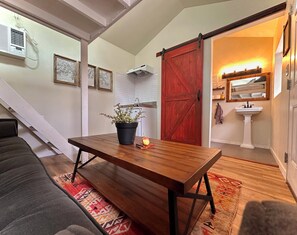 A cozy living area with a wooden table, a potted plant, and a red door leading to a bathroom.