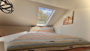 Un dormitorio con techo inclinado, tragaluz, cama con colcha estampada y un cuadro colgado en la pared.