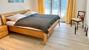 Ein Schlafzimmer mit einem hölzernen Bett, einem Nachttisch, einem Stuhl und einem Fenster mit Vorhängen.
