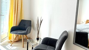 Ein modernes Zimmer mit grauem Sessel, einem kleinen Glastisch und einer Vase mit Trockenpflanzen.