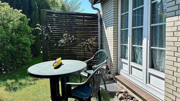 Eine Terrasse mit Tisch und Stühlen, ein Holzzaun und ein Haus mit großen Fenstern.
