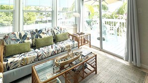 Et solbadet rum med en sofa, et glasbord og udsigt til en terrasse gennem store vinduer.
