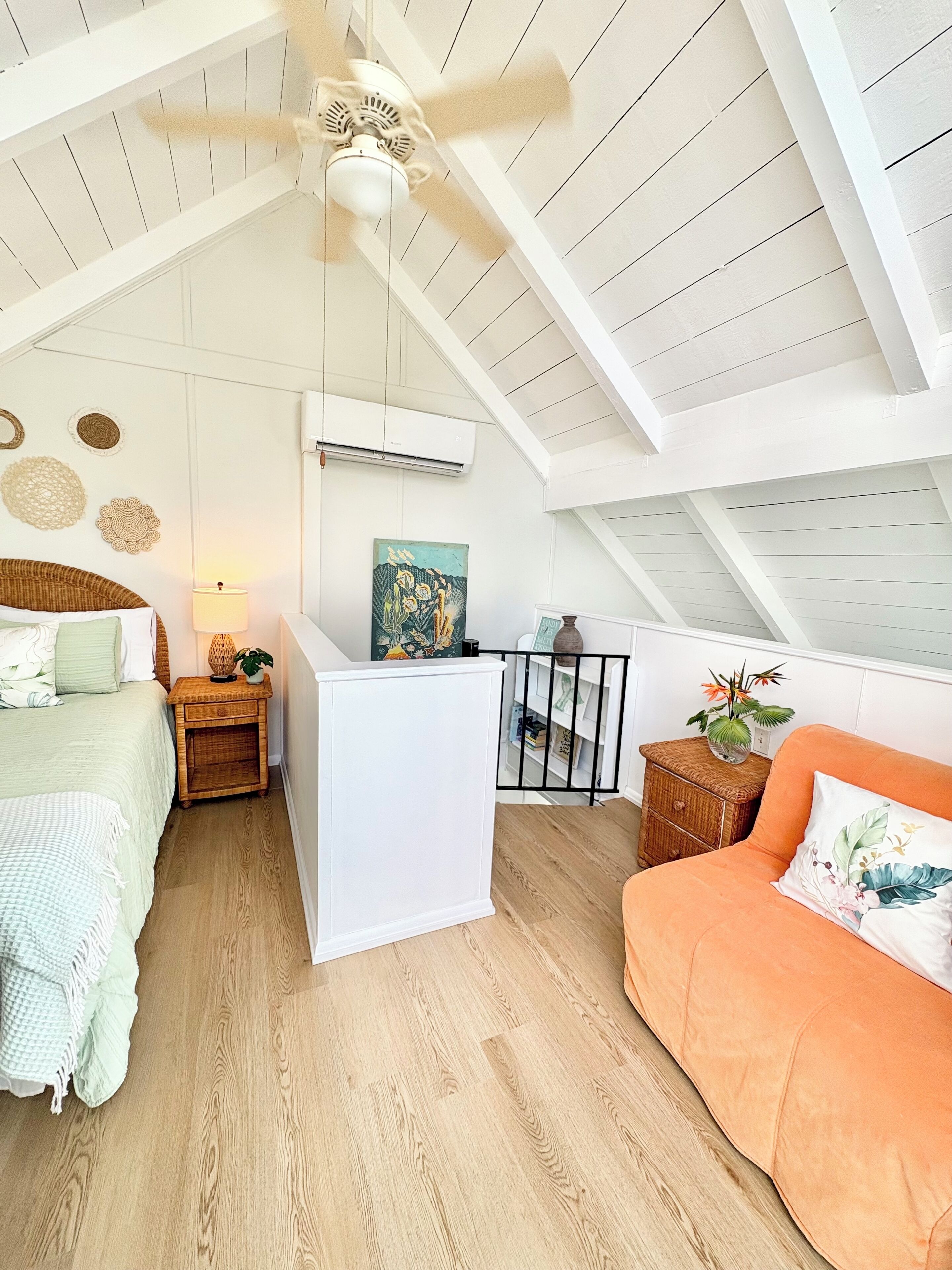 A cozy attic bedroom with a sloped ceiling, a bed, a small table with a lamp, a dresser, and a sofa.