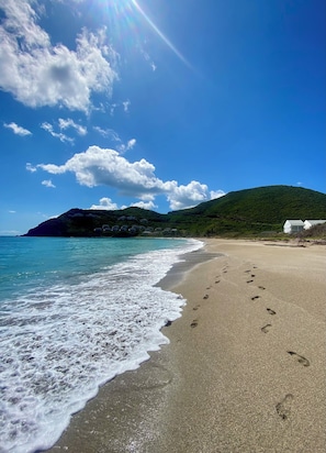 A beach with footprints leading to the water, a clear sky, and a hill in the background. - Seaside Charm: Steps to Beach, Bars, Taxi & Island Fun! (Frigate Bay 78Q7+6Q2 Kittian Village)