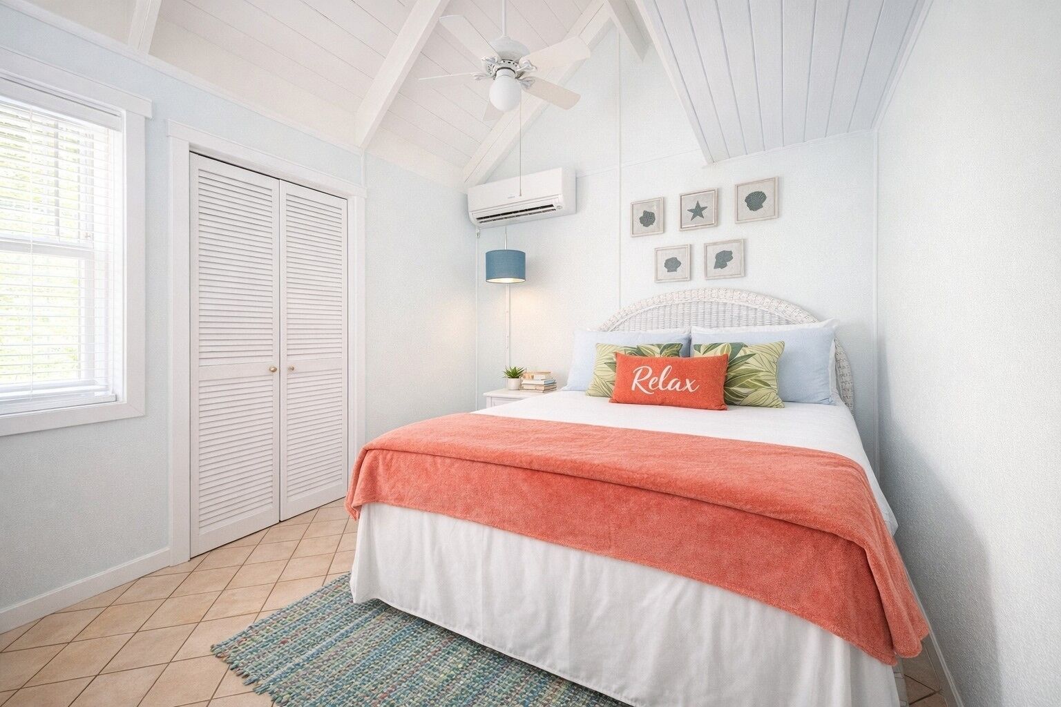 Une chambre à coucher comprenant un lit, un ventilateur de plafond, un appareil de climatisation, une fenêtre avec des stores et une porte.