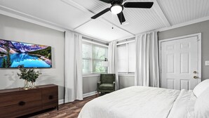 Una camera da letto con un letto, una cassettiera, una sedia, una ventola a soffitto e un televisore appeso al muro.