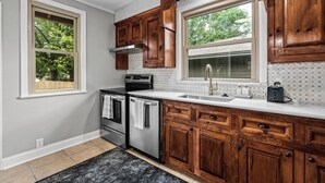 Una cucina con mobili in legno, piano cottura in acciaio inossidabile, lavello a due vasche e una finestra vista alberi.