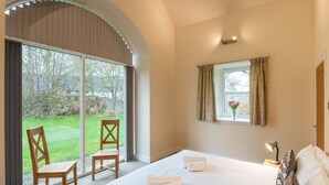 Ein Schlafzimmer mit einem großen Bett, zwei Stühlen, einem Fenster mit Vorhängen und Blick ins Freie.