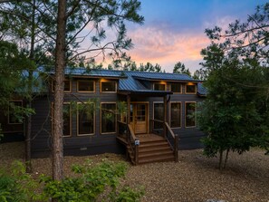 A two-story cabin with a porch, large windows, and a metal roof. - 🎶 Remedy of the Blues 🎶  · Chic Sanctuary: 2 King En-Suites & Hammock + Swing (Broken Bow)