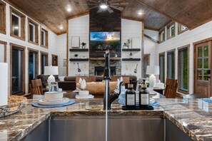 A spacious living room with a fireplace, a large TV, and a kitchen area with granite countertops and modern appliances. - 🎶 Remedy of the Blues 🎶  · Chic Sanctuary: 2 King En-Suites & Hammock + Swing (Broken Bow)