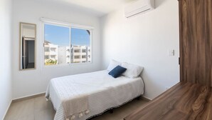 Une chambre à coucher comprenant un lit, une fenêtre, un appareil de climatisation et une armoire en bois.
