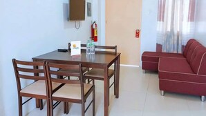 A dining area with a table and chairs, a television mounted on the wall, a fire extinguisher, and a red sofa. - Maple Residences (Talisay)