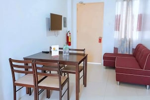 Un área de comedor con una mesa y sillas, un televisor montado en la pared, un extintor y un sofá rojo.