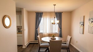 A dining area with a round table, four chairs, a chandelier, and a window with curtains. - Family-size condo in the heart of Fairbanks! Short walk to Creamer's field.  (Fairbanks)