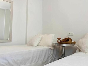 Two single beds with white bedspreads and matching pillows, a side table, and a large mirror.