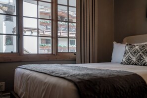 A bedroom with a large window, a bed with a patterned pillow, and a view of buildings outside. - Upscale Traditional Condo steps from Vail MTN w/ fireplace, hot tub + spa access (Vail)