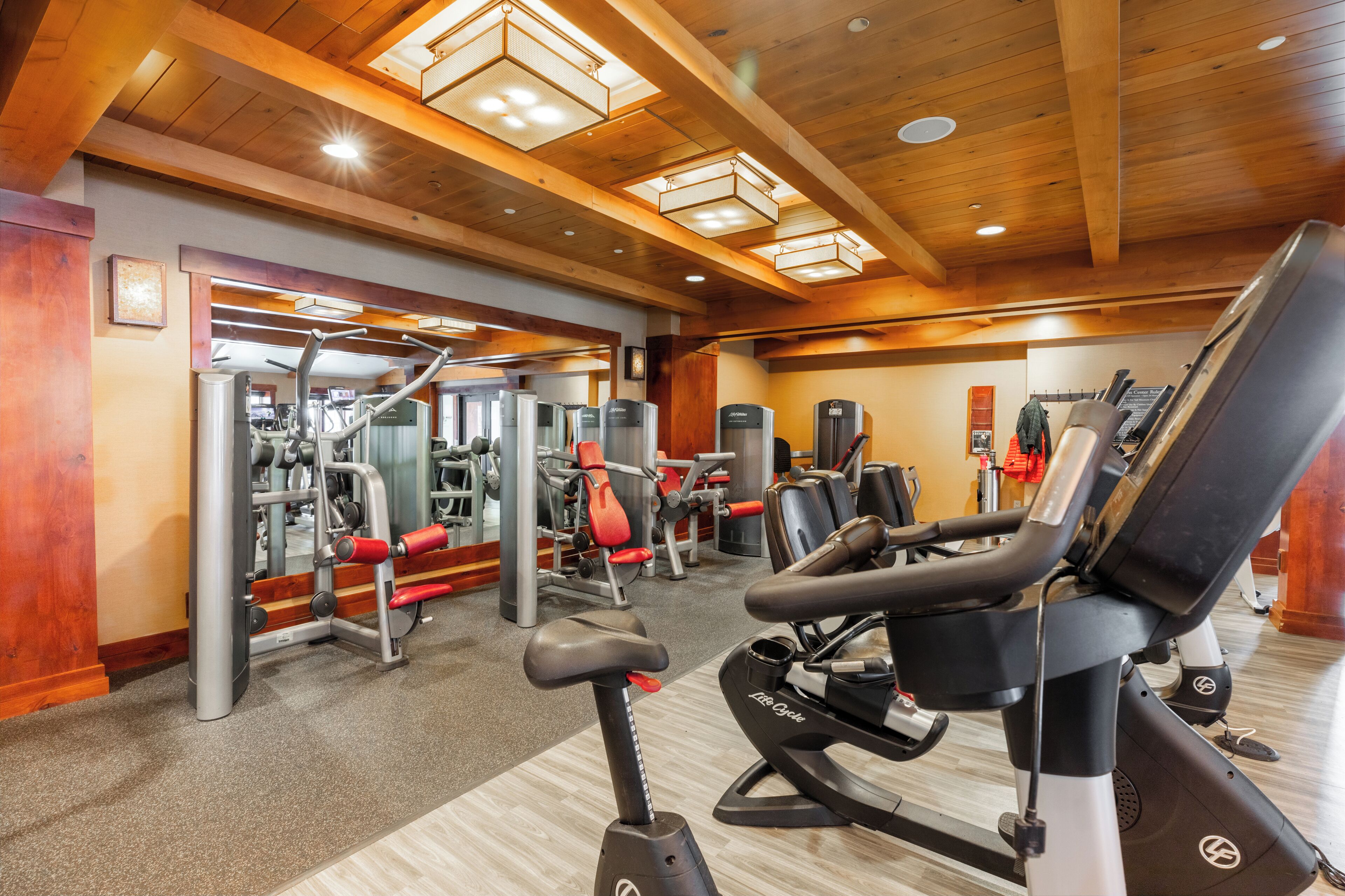 A gym with various exercise equipment, wooden ceiling beams, and a carpeted floor.